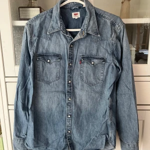 Levi's jeansskjorta - Säljer en blå jeansskjorta från Levi's Skjortan har två bröstfickor som kan stängas med knappar. Det går även att knäppa ärmarna vilket man kan se på sista bilden. Köptes för ca 800-900 kr💕