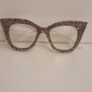 Glittriga cat eye-glasögon - Unika cat eye-glasögon med transparent båge täckt av färgglada glittrande stenar. Perfekt för dig som vill sticka ut och addera extra bling till din stil. Stora bågar med tydlig retrovibe och massor av attityd.