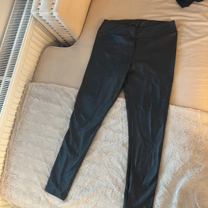 Svarta leggings i skinnimitation - Snygga svarta leggings med glansig finish som ger en skinnlook. Hög midja och tight passform, perfekta att styla med oversized tröjor eller crop tops. Mjukt och stretchigt material för maximal komfort.