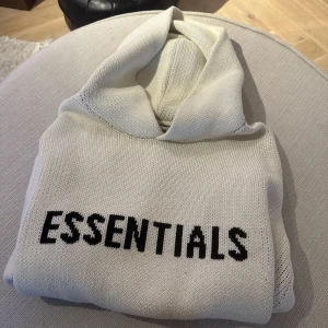Vit Essentials hoodie stickad M - Säljer en vit stickad hoodie från Fear of God Essentials i storlek M. Tröjan har svart ESSENTIALS-tryck framtill, huva och en clean, oversized vibe. Materialet är 60% bomull och 40% polyester, perfekt för dig som gillar streetwear med premiumkänsla. Den är boxig, så skulle säga att den är mer mot en large. 100% genuin, äkta.