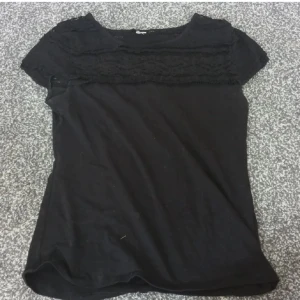 Svart blus med spetsdetaljer - Svart blus med korta ärmar och snygga spetsdetaljer över bröstet och axlarna. Rund halsringning och mjukt material som känns skönt mot huden. Perfekt för dig som gillar en stilren look med lite extra detaljer.