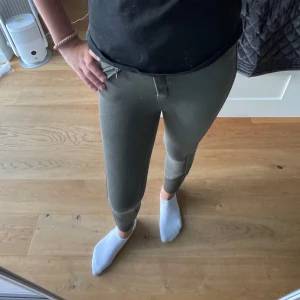 Gröna ridbyxor med dragkedja - Snygga gröna ridbyxor med tight passform och hög midja. Byxorna har en dragkedja vid fickan och grepp på insidan av benen för extra fäste i sadeln. Perfekta för dig som gillar ridning och vill ha stilrena, funktionella byxor.