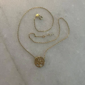 Guldhalsband med livets träd - Snyggt halsband i guldpläterat silver med ett runt hänge som har ett detaljerat livets träd-motiv. Hänget är stämplat med 925 vilket visar att det är äkta silver under guldpläteringen.