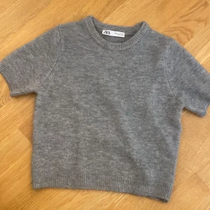 Grå stickad kortärmad tröja från Zara - Mysig grå stickad tröja från Zara med korta ärmar och rund hals. Perfekt för lager-på-lager och enkel att matcha med både jeans och kjol. Tröjan är i storlek S! Skriv för frågor eller fler bilder!☀️