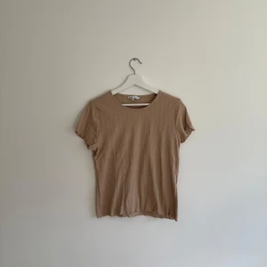 Beige ribbad topp från ONLY - Säljer en beige ribbad topp från ONLY i storlek L. Toppen har korta ärmar, rund halsringning och ett diskret mönster i tyget. Materialet är mjukt och stretchigt. 