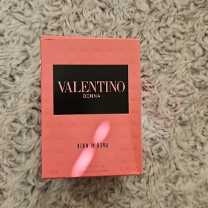 Valentino Donna Born In Roma EdP 100ml - Valentino Donna Born In Roma Eau de Parfum i en snygg rosa kartong med svart detalj. Flaskan rymmer 100 ml och är perfekt för dig som gillar lyxiga och feminina dofter. Förpackningen är tillverkad av kartong och har en modern, stilren design.