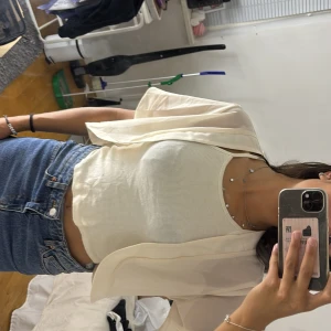 Ljusbeige transparent omlottväst - Säljer en ljusbeige, transparent väst med korta ärmar och omlottkänsla. Västen är croppad och har en luftig, flowy passform som ger en chill vibe. Perfekt att slänga över ett linne eller t-shirt för en extra touch.