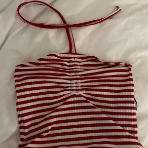 Randig halterneck topp från Pieces - Säljer en rödvit randig halterneck topp från Pieces i ribbad bomull. Toppen har smala ränder, knyt runt nacken och rynkade detaljer framtill. Perfekt för dig som vill sticka ut med en färgglad och trendig look.