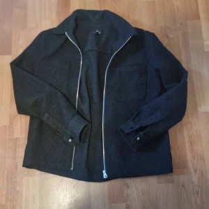 Svart overshirt från H&M i fleece - Svart overshirt från H&M i mjuk fleece med dragkedja framtill och klassisk krage. Jackan har en bröstficka och raka ärmar med knapp vid ärmslut. Perfekt för lager-på-lager och enkel att styla till streetwear. På bilden e jag 184 så den passar lite längre
