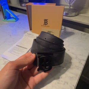 burberry bälte monogram - Säljer ett svart Burberry bälte i skinn med ikoniskt TB-monogram som spänne. Bältet har stilren design med präglad Burberry-logga på insidan och mattsvart metallspänne. Kommer med originalbox och kvitto. Perfekt accessoar för att lyfta din outfit. box kvitto dustbag till kommer bältet är ej använd och finns i endast storlek 105