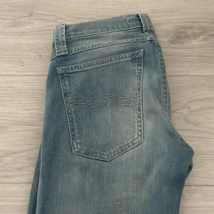 Nudie Jeans blå slim fit jeans - Säljer ett par klassiska blå jeans från Nudie Jeans i slim fit-modell. Jeansen är tillverkade av 100% ekologisk bomull samt Nudie Jeans signaturbrodyr på bakfickorna. Perfekta för dig som gillar en avslappnad men stilren look.