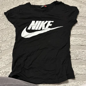 Svart Nike t-shirt med logga - Svart t-shirt från Nike med stor vit logga och swoosh på bröstet. Klassisk rund halsringning och korta ärmar. Perfekt för en sportig och avslappnad stil.