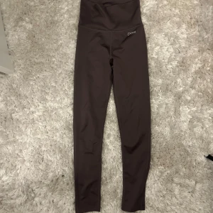 Brun/lila träningstights från Drop of Mindfulness - Mörkbruna/lila, höga tights från Drop of Mindfulness med diskret logga framtill. Tillverkade i stretchigt material. Perfekta för träning eller chill dagar, sitter tajt och bekvämt i midjan. Säljer då de inte passar🌸🌸