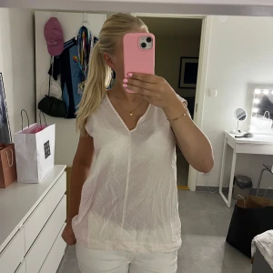 Ljusrosa blus med v-ringning - Söt ljusrosa blus från Boomerang med små prickar, v-ringning och ärmlös design. Lätt och luftig i bomullsmix, perfekt för varma dagar. Nyckelhålsöppning bak i nacken ger en extra detalj. Enkel att matcha med jeans eller kjol.