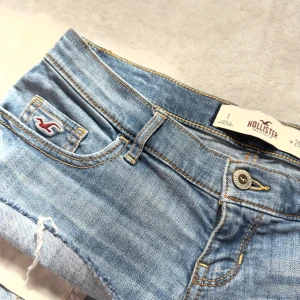 Ljusblå jeansshorts från Hollister - Snygga ljusblå jeansshorts från Hollister. Shortsen har låg midja, slitna detaljer och Hollisters logga på fickan. Perfekta för varma dagar och en avslappnad stil.