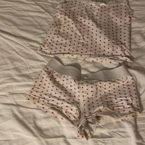 Vita shorts och tröjamed röda hjärtan Gina Tricot - Supersöta vita shorts från Gina Tricot med små röda hjärtan över hela tyget. De har bred resår i midjan och knappar framtill. Perfekta för sommaren och riktigt gulliga detaljer. Mjukt och skönt material.