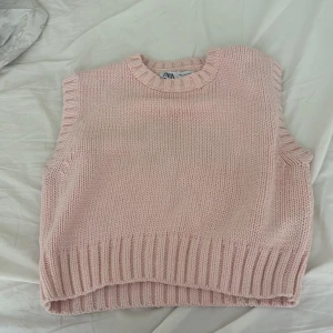Ljusrosa stickad väst från Zara - Superfin ljusrosa stickad väst från Zara med bred ribbad kant vid hals, ärmhål och nederkant. Västen har en klassisk, boxig passform och är perfekt att styla över en skjorta eller t-shirt för en trendig look.