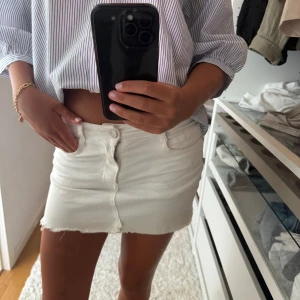 Vit jeanskjol - Snygg vit kort jeanskjol med fransig kant nertill. Klassisk femficksmodell med knapp och dragkedja framtill samt bälteshällor. Perfekt till sommarens alla outfits och enkel att matcha med allt.