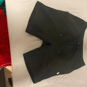 Svarta shorts från Polo Ralph Lauren - Svarta shorts från Polo Ralph Lauren med klassisk vit broderad logga framtill. Modellen har snörning i midjan och en bakficka. Sköna och stilrena, perfekta för sommaren eller chill dagar. Materialet är mjukt och känns som bomull.