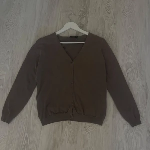 Brun kofta med v-ringning - En enkel brun kofta  med v-ringning och knappar framtill. De är en långärmad modell i mjukt material och den har ribbad mudd vid ärmslut och nederkant. Superfin och perfekt att ha över en t-shirt eller ett linne!