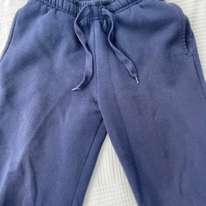 Mörkblå mjukisbyxor från Gina Tricot - Mörkblå mjukisbyxor från Gina Tricot med dragsko i midjan och elastisk resår. Byxorna är tillverkade i mjukt material och har en avslappnad passform, perfekta för chill dagar. Klassisk design utan synliga loggor på benen.