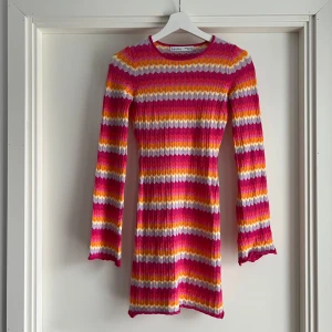 Viral randig stickad klänning från Bershka - Trendig slutsåld färgglad kort stickad klänning från Bershka med vågiga ränder i rosa, lila, orange, gul och vit. Långärmad modell med öppen rygg och knytband. Ribbad struktur som sitter snyggt på kroppen. Perfekt för dig som vill sticka ut med en lekfull look. Aldrig använt. 