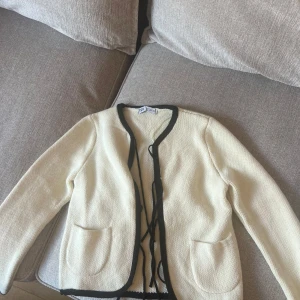 Vit stickad från Zara med svarta detaljer - Snygg vit stickad från Zara med svarta kanter och knytband framtill.  Säljer då den ej kommer till användning. Använd få gånger, storlek L men passar mig som har S då den var liten i storleken!