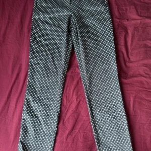 Svarta byxor med grafiskt mönster - Snygga svarta byxor med vitt grafiskt mönster över hela tyget. Byxorna har rak passform och resår i midjan för extra komfort. Perfekta för dig som vill sticka ut lite extra med din outfit.