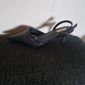 Svarta pumps med spetsig tå från Nelly - Snygga svarta pumps från Nelly med spetsig tå, låg klack och dubbla remmar med små nitar. 