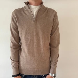 JOHN HENRIC HALF ZIP TRÖJA - Snygg beige stickad tröja från John Henric med half zip-dragkedja och hög krage. Perfekt för lager-på-lager och passar till både jeans och chinos. Långärmad och i mjukt material som känns skönt mot huden. 100% merinoull lyxigt material. 