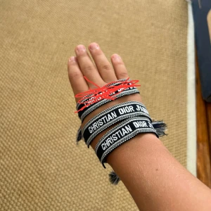 2 st Christian Dior svart/vitt armband - Snyggt armband från Christian Dior i svart och vitt med tydlig logga. Armbandet är gjort i vävd textil och har coola tofsar i ändarna. Perfekt accessoar för att lyfta din outfit med en exklusiv touch.