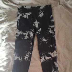 Svarta leggings med vit mönster - Säljer ett par svarta leggings med coolt vitt mönster som påminner om blixtar. Hög midja och scrunch-detalj bak för extra passform. Perfekta för gymmet eller chill dagar. De ser väldigt små ut men de är ett väldigt stretchigt material som sitter skönt och följer kroppen. 