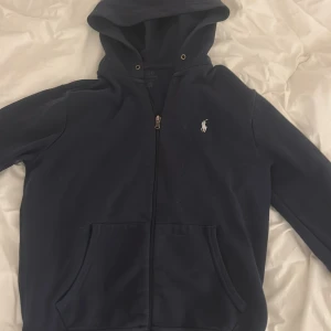 Marinblå hoodie från Polo Ralph Lauren - Snygg marinblå hoodie från Polo Ralph Lauren med dragkedja och klassisk vit logga på bröstet. Tröjan har huva, känguruficka,pris kan diskuteras 🥰