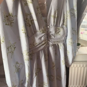 Klänning ginatricot - Superfin ljusblå klänning med blommigt mönster och v-ringning. Klänningen har långa ärmar, markerad midja med knappar. Helt oanvänd med lapp kvar! Storlek S och inga fläckar. Köpt för 550