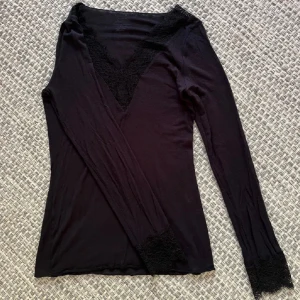 Svart långarmad topp med spets från Intimissmi - Supersnygg svart långarmad topp från Intimissmi med v-ringning och spetsdetaljer vid halsringning och ärmslut. Tunn och mjuk kvalitet i bomull och kashmir, perfekt för lager-på-lager eller som statement-piece. Sitter tight och har en elegant vibe. Bara ett litet hål i nedre delen av armen inget som syns❤️