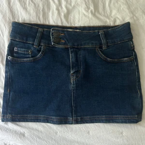 Mörkblå jeanskjol - En mörkblå mini jeanskjol med bakfickor och dubbla knappar framtill. Knappt använd 