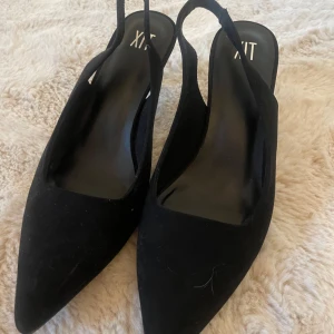 Svarta klackskor med spetsig tå - Svarta klackskor från din sko med elegant spetsig tå och öppen häl. Skorna har en klassisk hög klack och är tillverkade i mockaliknande material som ger en lyxig känsla. Perfekta för att lyfta vilken outfit som helst.nypris. 499
