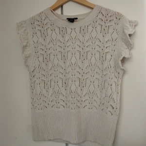 Vit stickad ärmlös topp med volang - Supersöt vit stickad topp med volangdetaljer vid axlarna. Den passar mig perfekt som har storlek M i plagg. Inga defekter och har använts fåtal gånger❤️