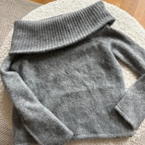 Grå stickad offshouldertröja Pieces - Supermysig grå stickad tröja från Pieces med bred ribbad krage som kan bäras offshoulder. Perfekt för lager-på-lager och chill höst- eller vinterstil. Långärmad och i mjukt material som känns skönt mot huden.