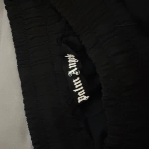 Palm Angels svarta shorts med vita ränder - Svarta shorts från Palm Angels med vita ränder längs sidorna och broderad logga på vänster ben. De har elastisk midja och sportig look, perfekta för en chill streetwear-stil. Materialet är mjukt och följsamt, troligtvis polyester. Säljer då dem inte passar mig använda 1 gång 