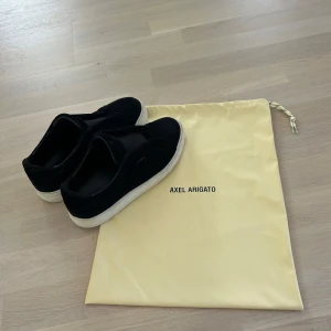 Axel arigato 360 laceless - Stilrena svarta sneakers från Axel Arigato i mocka med vit platt sula. Slip-on-modell utan snörning, perfekt för en clean och modern look. Kommer med original dustbag. 