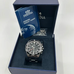 Festina kronograf herrklocka - Stilren herrklocka från Festina med svart urtavla, silverfärgade detaljer och kronograf-funktion. Klockan har robust länkarmband i metall och tydliga indexmarkeringar. Kommer i originalask med extra länkar och garanti. Perfekt accessoar för dig som gillar sportig och klassisk stil.