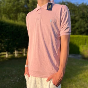 Ljusrosa pikétröja från Polo Ralph Lauren Size Small - Snygg ljusrosa pikétröja från Polo Ralph Lauren med klassisk krage, tre knappar och broderad logga på bröstet. Tillverkad i mjuk bomull som andas, perfekt för varma dagar. Enkel och stilren design som passar till det mesta. Den är också sprillans ny och det är lite sportigt material perfekt för sommaren och den passar mer som small🙌