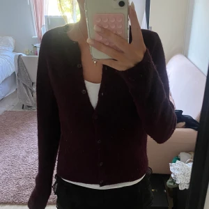 Vinröd kofta med knappar - Säljer en mysig vinröd kofta med knappar framtill. Koftan har lång ärm och är stickad i ett mjukt material som passar perfekt till lager på lager. Enkel och stilren design som är lätt att matcha med olika outfits.