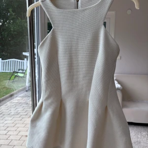 Vit topp - Supersnygg vit topp från Gina Tricot med strukturerat tyg och markerad midja. Ärmlös modell med rund halsringning och dragkedja i ryggen. 