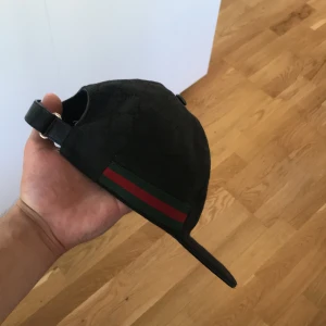 Svart Gucci keps med GG-mönster - Snygg svart keps från Gucci med klassiskt GG-monogram över hela kepsen och ikoniska gröna och röda ränder på sidan. Justerbar rem bak i svart skinn och diskret Gucci-märke. Äkta , utan box. Storlek M 