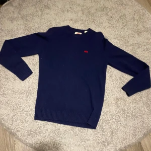 Mörkblå stickad tröja från Levi's XS helt ny - Snygg mörkblå stickad tröja från Levi's i storlek XS. Klassisk modell med rund halsringning, ribbade muddar och liten röd Levi's-logga på bröstet. Perfekt för dig som gillar enkel och stilren look.