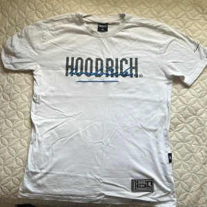 Vit t-shirt från Hoodrich med tryck - Vit t-shirt från Hoodrich i bomull med stort tryck på bröstet och ryggen. Klassisk passform med korta ärmar och rund hals. Snygga blå och svarta detaljer i trycket samt patch nertill. Perfekt för dig som gillar streetwear vibes.