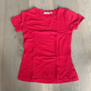 Röd t-shirt från Kappahl XS - Enkel och stilren röd t-shirt från Kappahl i storlek XS. Modellen är klassisk med rund halsringning och korta ärmar. T-shirten är gjord i mjuk bomull och har en figurnära passform som sitter super snyggt.