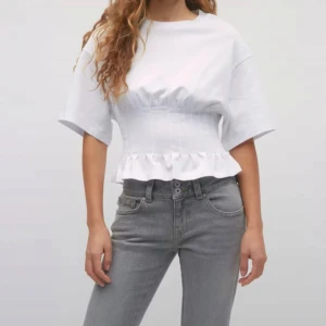 Vit  topp från Gina Tricot - Superfin vit topp från Gina Tricot med volang nedtill och markerad midja. T-shirten har korta ärmar och rund hals. Perfekt för dig som gillar en feminin och trendig look.🫶🏻👩🏼‍❤️‍💋‍👨🏼Aldrig använd!🙌🏼